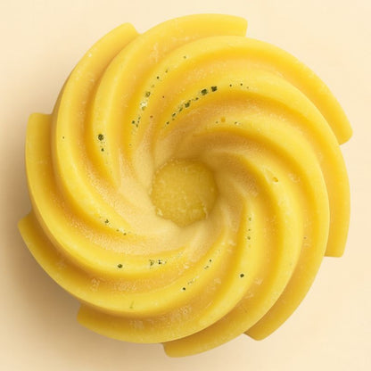Fondant Parfumé Spirale Monoï, de couleur jaune avec des paillettes, de forme spirale et sur fond beige clair.