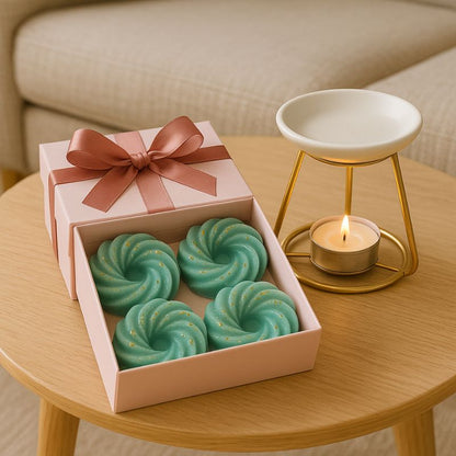 Fondant Parfumé Spirale Sapin de Noël, présenté dans un coffret-cadeau avec un nœud et il y a un brûleur juste à côté, le tout posé sur une table basse en bois.