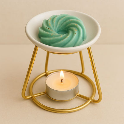 Fondant Parfumé Spirale Sapin de Noël, disposé dans un brûleur doré et allumé avec une bougie chauffe-plat. Sur fond beige