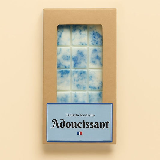 Fondant Parfumé Tablette Linge Propre, de couleur bleue et le parfum est adoucissant, dans sa boîte de conservation. Sur fond beige clair.