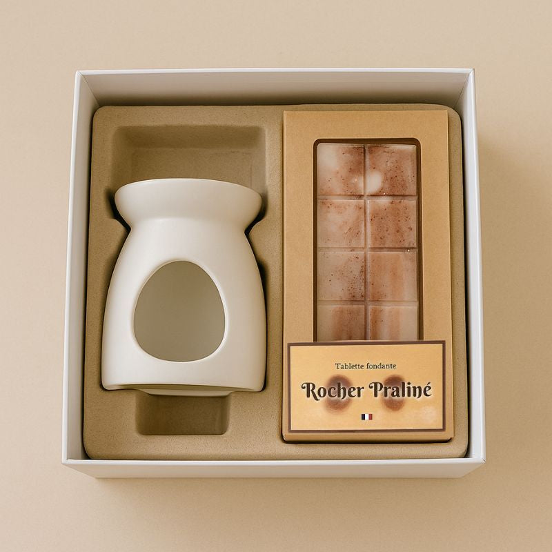 Fondant Parfumé Tablette Rocher Praliné, présenté dans un coffret cadeau avec un brûleur et la tablette de fondant parfumé. Sur fond beige clair.
