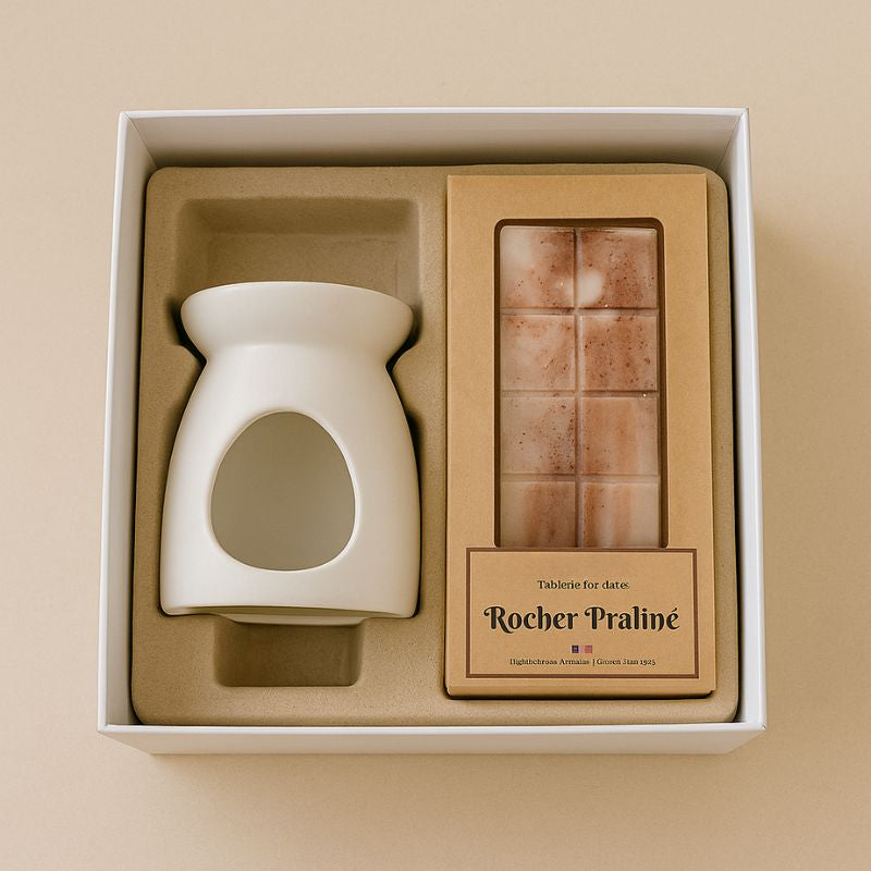 Fondant Parfumé Tablette Rocher Praliné, présenté dans un coffret cadeau avec un brûleur et la tablette de fondant parfumé. Sur fond beige clair.