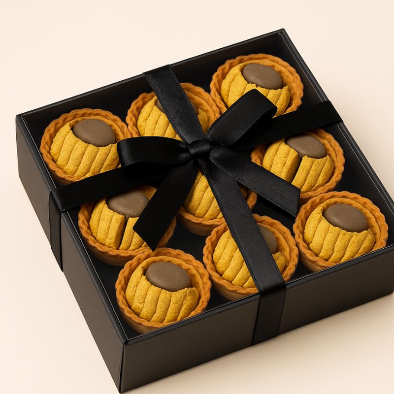 Fondant Parfumé Tartelette Châtaigne Grillé, présenté dans un coffret-cadeau noir avec un noeud. Sur fond beige.