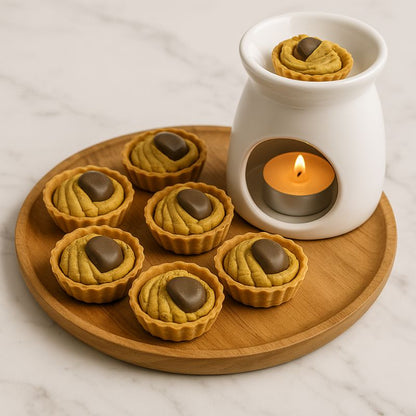 Fondant Parfumé Tartelette Châtaigne Grillé, un brûleur posé sur un plateau en bois et avec des fondants posé dessus. Le tout posé sur une table en marbre.