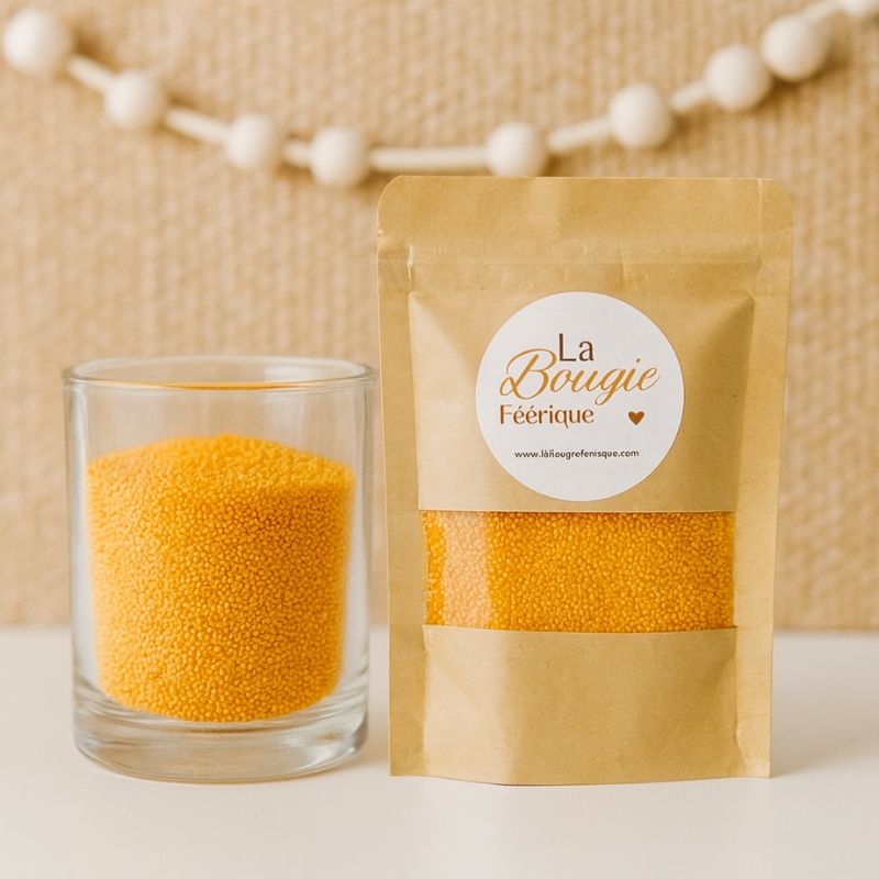 Perles de Cire Décorative pour Bougie, de couleur orange, avec son contenant transparent où il y a de la cire perle en démonstration. Fond beige.