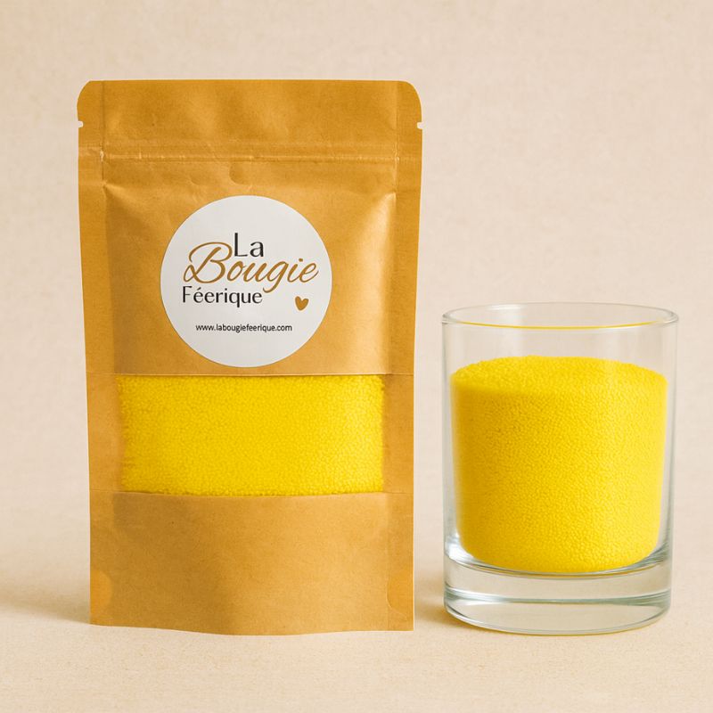 Perles de Cire Décorative pour Bougie, de couleur jaune, avec son contenant transparent où il y a de la cire perle en démonstration. Fond beige.
