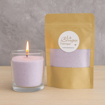 Perles de Cire Décorative DIY, de couleur violette, avec son contenant en verre et la bougie est allumée. Sur fond gris.