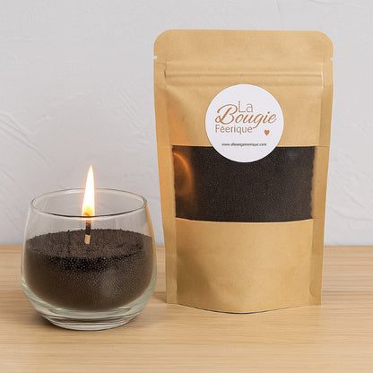 Perles de Cire Décorative DIY, de couleur noire et avec son contenant en verre, la bougie est allumée. Sur fond gris.