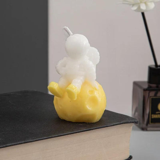 Bougie Décorative Astronaute, de couleur jaune, posée sur un livre noir et sur fond beige.