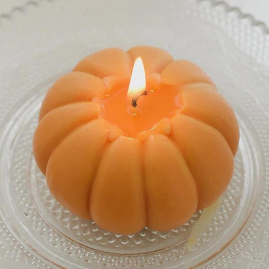 Bougie Décorative Fruit Citrouille, allumée et disposée dans une couple sur une table.