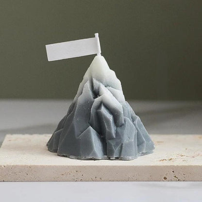 Bougie Décorative Iceberg, de couleur grise, disposée sur un plateau en marbre et sur une table blanche. Fond vert foncé.