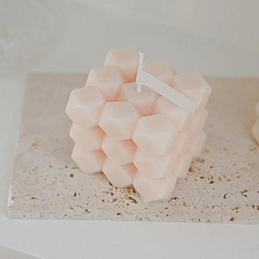 Bougie Parfumée Cube Diamant, de couleur rose et posée sur une table.